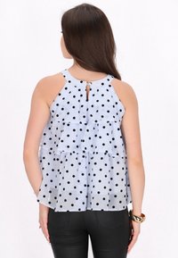 Top senza maniche azzurro chiaro con pois neri, design a strati, scollatura rotonda e dettaglio a apertura a chiave sul retro. Abbinato a pantaloni neri.