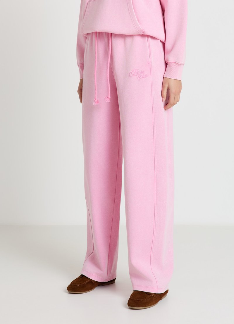 Pantalon de survêtement rose en matériau doux, avec des bandes latérales, une taille ajustable à cordon et un logo subtil brodé à l'avant.