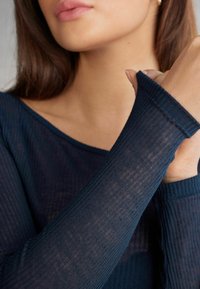 Granatowa bluzka z długim rękawem, prążkowana, z szerokim dekoltem i dopasowanymi mankietami, z teksturowanego, przezroczystego materiału, co tworzy delikatny efekt warstwowy.