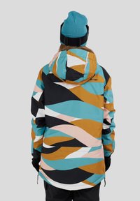 Kolorowa kurtka z abstrakcyjnymi wzorami w turkusie, pomarańczu i różu. Materiał wydaje się gładki; posiada kaptur i regulowane mankiety.