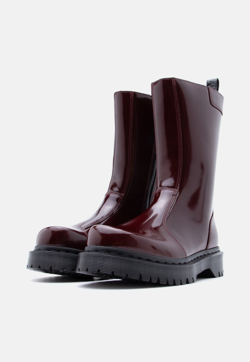 Bottes chevilles bordeaux brillantes avec une finition lisse, dotées d'une semelle noire épaisse et d'une fermeture éclair latérale pour un enfilage facile. Semelle extérieure texturée pour une bonne adhérence.