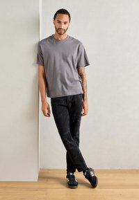 Gray cotton t-shirt with short sleeves, paired with black jeans featuring a subtle pattern. Black sneakers with white accents complete the look.