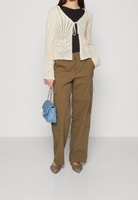 Virkat kardiagan i gräddvit med knytskärp, kombinerat med olivgröna cargo-byxor och silverfärgade spetsiga lägenheter; håller en liten blå handväska.