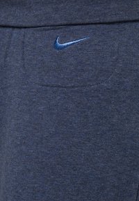 Tmavě modrá bavlněná směs s jemnou texturou; nad přední kapsou je malý modrý vyšívaný logo Nike.