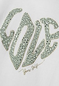 Biała koszulka z tkaniny z napisem "LOVE" w zielonym wzorze lamparta z złotą obwódką, a poniżej tekst "Your Self" w stylu odręcznym.