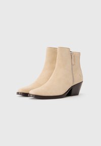 Stivaletti ankle in suede beige con punta affusolata, cerniera laterale e tacco a blocco marrone scuro. Texture liscia con un design minimalista.