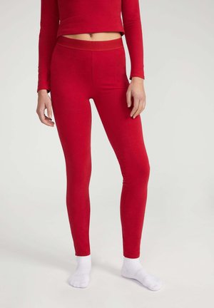 Maglietta rossa a maniche lunghe e leggings abbinati in tessuto misto cotone, con un design aderente e una texture liscia. Calzini bianchi a caviglia visibili.
