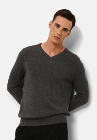 Dunkelgrauer Strickpullover mit V-Ausschnitt, Rippbündchen und langen Ärmeln. Das Material wirkt weich mit einer glatten Textur.
