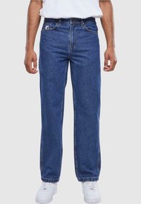 Blå denim jeans med en rette ben-design, standard lommer og en subtil logo på linningen. Brukt med hvite treningssko.