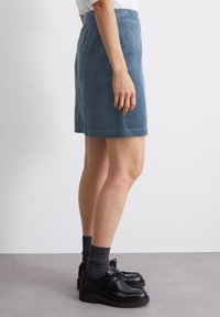 Modra kordna krila s ravnim krojem, z elastičnim pasom in kontrastnim šivom. Združena z črnimi čevlji in sivimi nogavicami.