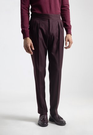 Pantalones burdeos con pliegues, de cintura alta y con una textura suave, combinados con zapatos de cuero oscuros con un diseño trenzado.