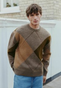 Brown knitted sweater with a geometric argyle pattern in shades of brown and green. Ribbed crew neckline and cuffs, paired with denim jeans.