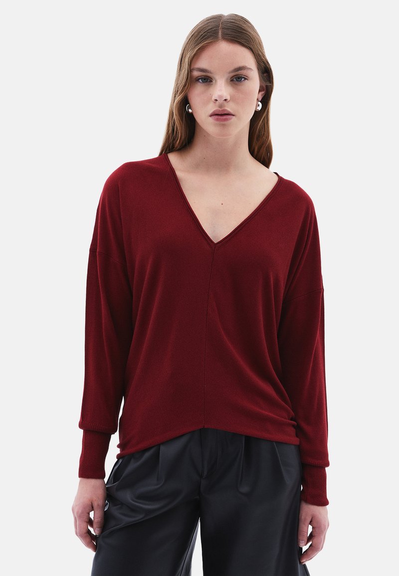 Maglione bordeaux a V con maniche lunghe e polsini a coste, realizzato in tessuto morbido. Presenta una vestibilità comoda e un delicato dettaglio di cucitura centrale.