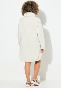 Helle beigen Hoodie-Kleid mit hohem Kragen, Raglanärmeln und seitlichen Schlitzen. Kombiniert mit mehrfarbigen Sport sneakers. Glatte Textur.