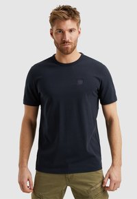 Camiseta de algodón azul marino con mangas cortas, cuello redondo y un pequeño parche de logo texturizado en el pecho. Textura suave, corte clásico.