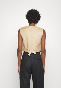 Beige Leinen ärmelloses Oberteil mit einer Krawattendetails am Rücken, kombiniert mit schwarzen Leinenhosen mit einer Gesäßtasche. Einfaches, figurbetontes Design.