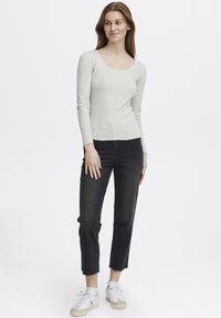 Lys grå langermet topp med dyp utringning, paret med høytlivs svarte jeans med råkant i kanten og hvite sneakers.