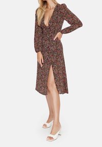 Blommig klänning med långa puffärmar, djup V-hals och sidodel. Har en mörk bakgrund med färgglada små blommor, i kombination med vita klackar.