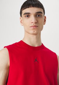 Piros ujjatlan póló, pamutból készült, fekete Air Jordan logóval a mellkasán, kerek nyakkivágással és sima, könnyű anyaggal.