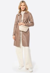 Bruine leren knoopjasje, beige crossbody tas met rits, crèmekleurige coltrui en witte broek met wijde pijpen, gecombineerd met witte sneakers.