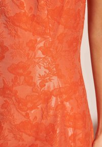 Πορτοκαλί ύφασμα με κέντημα λουλουδιών και διαφάνεια, που παρουσιάζει περίπλοκα μοτίβα φύλλων και λουλουδιών, δημιουργώντας ένα ιδαίτερο δίδυμο εφέ.