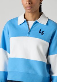Sudadera a rayas azules y blancas con cuello con cremallera, que presenta un pequeño logo "LS" bordado en el pecho. Material suave de algodón.