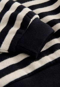 Tissu tricot rayé noir et blanc avec un gros plan d'un poignet de manche plié en tricot côtelé noir uni.