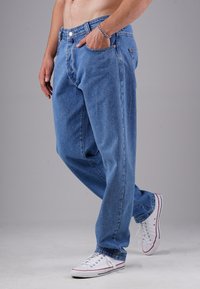 Hellblaue Jeans aus Denim mit lockerer Passform, fünf Taschen, Knopf- und Reißverschluss sowie kontrastierenden Nähten. Kombiniert mit weißen Sneakers.