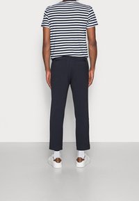 Koszula w paski z krótkim rękawem w kolorze granatowym i białym, zestawiona z jednolitymi ciemnymi spodniami z bocznymi kieszeniami oraz białymi trampkami z brązowymi detalami.