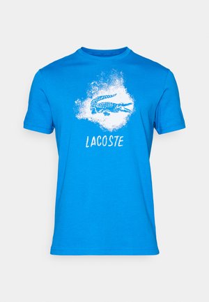 Blue t-shirt made of cotton featuring a white graphic of a crocodile and the word "LACOSTE" below. Short sleeves and a crew neck design.