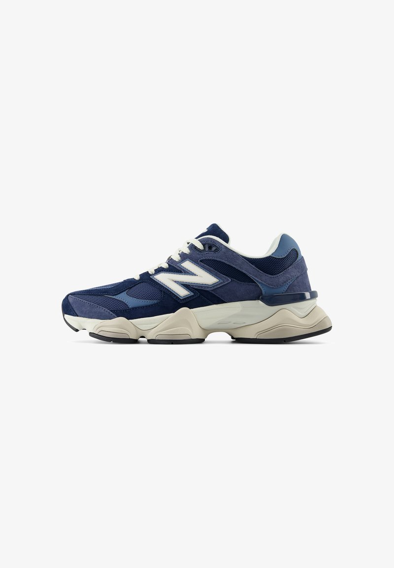 Chaussure de sport New Balance bleu foncé avec des lacets blancs, des empiècements en mesh et en daim, et une semelle épaisse beige.