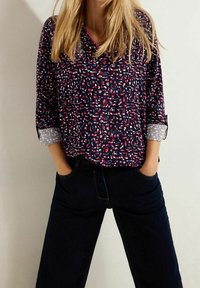 Blouse à motif marine avec des formes abstraites en rose et blanc, dotée de longues manches retroussées aux poignets dans un motif clair contrastant.