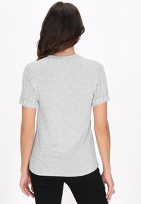 Grå kortærmet t-shirt, ribbet detaljer på ærmerne, afslappet pasform, blød tekstur, rund halsudskæring, båret med sorte bukser, set fra ryggen.