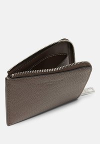 Portefeuille en cuir brun texturé avec une fermeture éclair en argent, doté de deux compartiments et d'une boucle pour étiquette. Design minimaliste avec des lignes épurées.