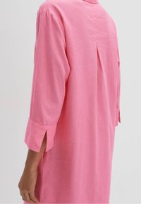 Rosa långärmad tunika skjorta, tillverkad av lättviktsmaterial, med krage, sidoflikar och en veckdetalj på baksidan.