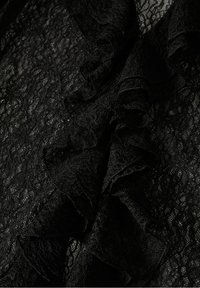 Tissu en dentelle noire avec un motif floral complexe et une texture froncée, montrant une délicate transparence et des coutures détaillées.