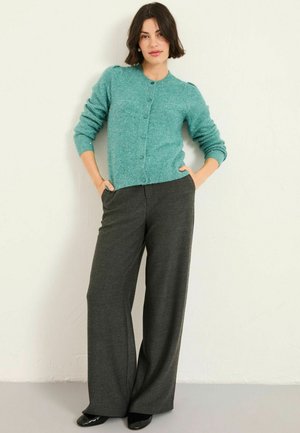Teal gestrickte Strickjacke mit Knopfverschluss und gerippten Ärmelbündchen, kombiniert mit grauen weit geschnittenen Hosen mit strukturiertem Muster.