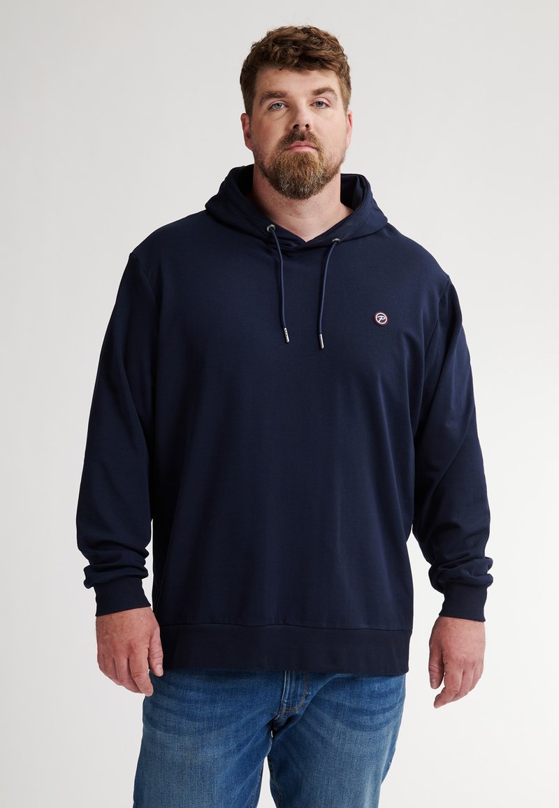 Felpa blu navy con tasca frontale, cordini e un piccolo logo. Tessuto morbido e vestibilità ampia, abbinata a jeans in denim blu.