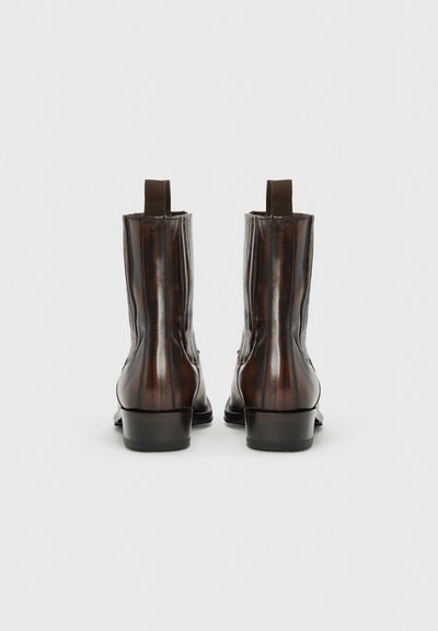Botas de tobillo de cuero marrón con un acabado brillante, paneles laterales elásticos y un tacón pequeño. Presentan rayas verticales y lengüetas en la parte trasera.