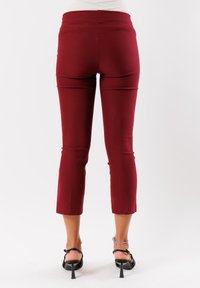 Pantaloni capri bordeaux con un design aderente e una cintura elastica, caratterizzati da bordi orlati e una texture liscia e elasticizzata.