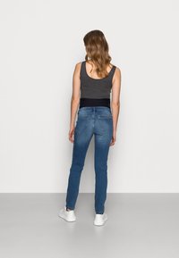 Jeans de ganga em azul claro com design ajustado e cinco bolsos. Com um cós preto. Ténis brancos completam o visual.