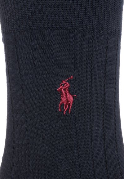 Chaussette côtelée bleu marine avec un logo de joueur de polo rouge brodé au niveau du poignet. Fabriquée en matériau doux et extensible pour un confort optimal.
