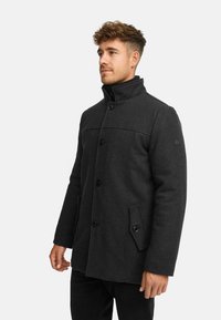 Mørkegrå uldfrakke med høj krave, knaplukning foran og sidelommer. Glat tekstur med en skræddersyet pasform og minimalistisk design.