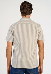 Koszula z krótkim rękawem w jasnobeżowym kolorze z pionowymi paskami i fakturowanym wzorem. Posiada klasyczny kołnierzyk oraz boczne rozcięcia na dole.