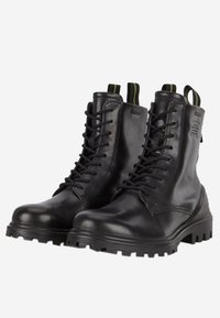 Botas de cuero negro con cordones, punta redonda, suela de goma gruesa, costuras reforzadas y lengüetas con toques de verde en contraste.