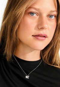 Sidabrinė vėrinio grandinėlė su trimis lapeliais, puošta blizgiu paviršiumi, dėvima ant juodos palaidinės. Lapų lapeliai turi subtilių detalių.