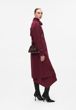 Burgundy wool coat with a collar, belted waist, and long sleeves; paired with black stiletto boots and a brown handbag with a chain strap.