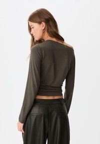 Mørkegrøn langærmet top med en rund halsudskæring og en tætsiddende silhuet, parret med højtaljede sorte læderbukser. Glat stofstruktur.