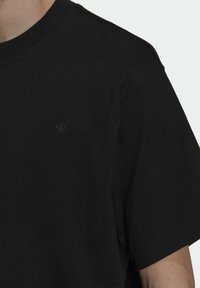 Svart t-shirt i bomull med korta ärmar, med en tonalt broderad logotyp på bröstet. Rund hals och strukturerad tyg.