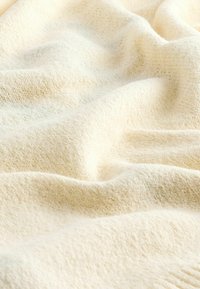 Manta de crema suave con una superficie texturizada, que presenta un patrón tejido ligero y suaves pliegues, enfatizando su aspecto acogedor y atractivo.